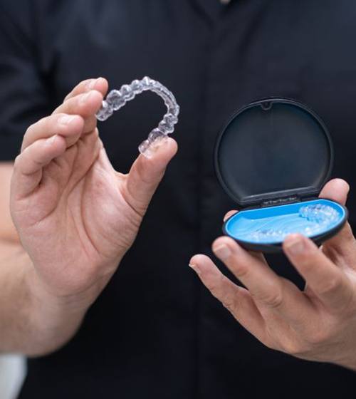 Man in scrubs holding clear aligners