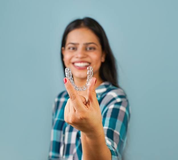 Smiling woman holding clear aligners